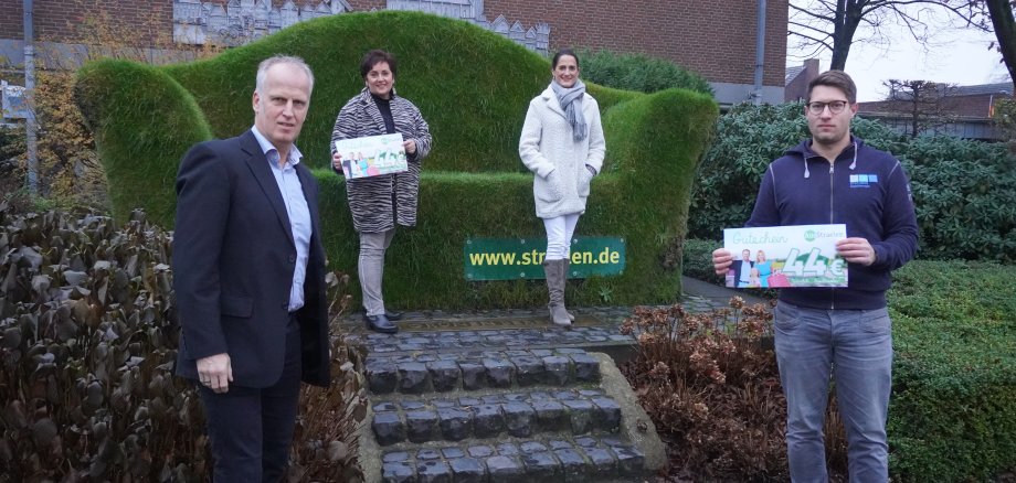 Uwe Bons, Klaudia Werdin, Marta Sommerkamp und Jan van de Stay (v.l.) präsentieren den neuen 44 Euro Gutschein der Unternehmergemeinschaft AusStraelen vor der Grünen Couch.